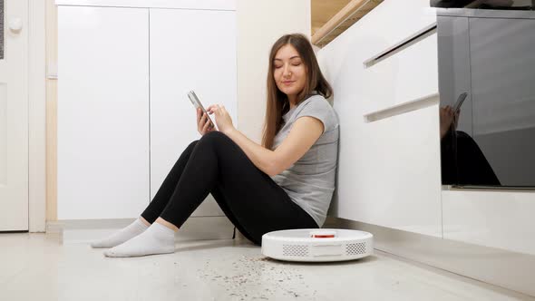 Woman with Phone on Floor Robot Vacuum Cleaner Removes Dirt