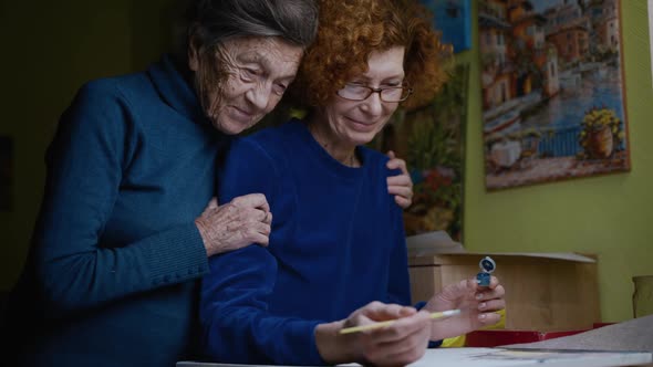 Senior Couple 90 Years Old Mom and Older Daughter Hug and Painting