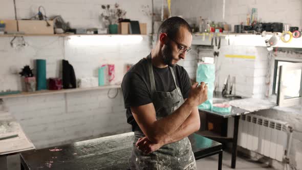 Male portrait: man smokes a cigarette in a workshop. The sculptor is tired and resting.