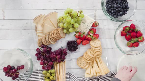 Flat lay. Step by step. Arranging cheese platter with fresh fruits, gourmet cheese, and crackers.