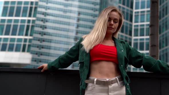 a Blonde Woman in a Red Top and Green Shirt Poses Against a Backdrop of High-rise Buildings. Bottom