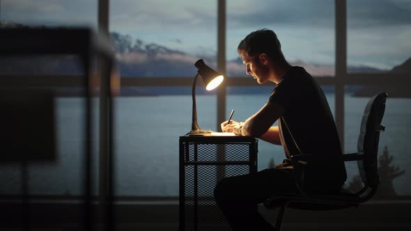 Serious Concentrated Young Male Student Studying at Home Office Sitting in Cozy Workplace at Night