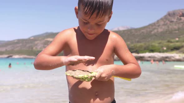 Close up slow motion on cute caucasian greek child, filling a toy shovel with brown sand, beautiful