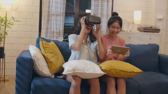 Asian female feeling happy using laptop and VR playing games together while lying sofa.