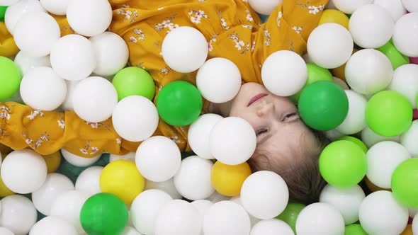 a Little Girl Plays in a Dry Pool with White Yellow and Green Plastic Balls