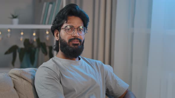 Thoughtful Arabic Pensive Indian Adult Bearded Man Sitting on Sofa at Home in Evening Looking Away