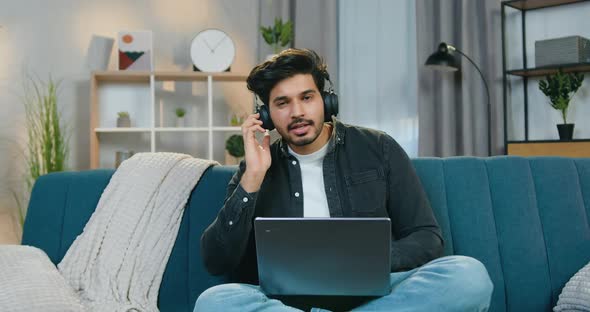 Guy in Earphones Sitting on the Sofa at Home and Enjoying Favourite Music Singing Songs into Camera