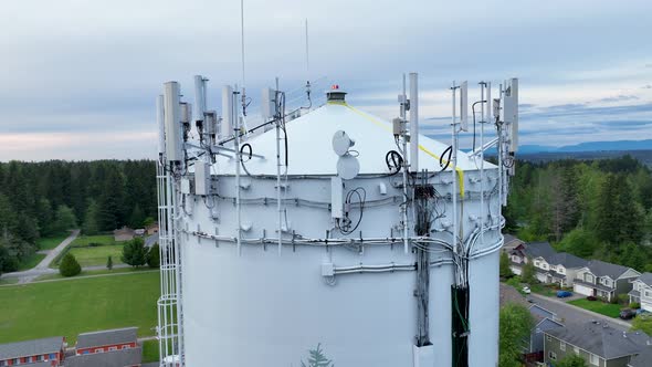 Close up aerial shot of the many pieces of telecommunication equipment on top of a water tower.