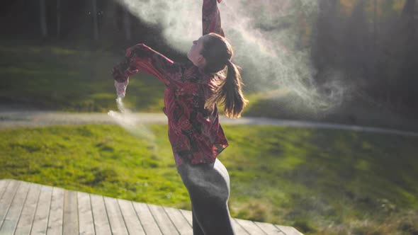Slow motion of a young woman throwing white powder on a wooden platform at golden hour sun set. Sun