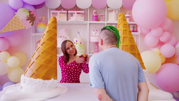 Beautiful Woman Holding Out Muffin with Lighting Candle to Man in Confectionery