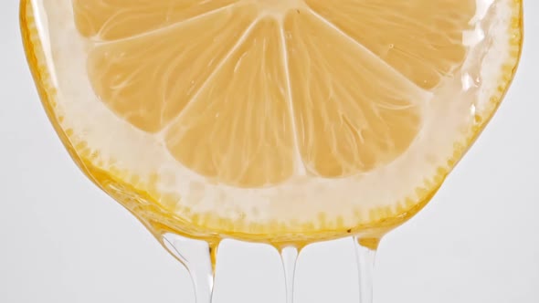 Macro Shot of Flowing the Juice and Oil Stream From Lemon Slice on White Background