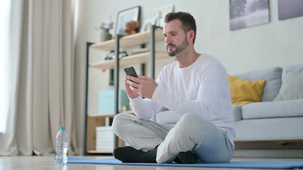 Man Using Smartphone on Yoga Mat at Home