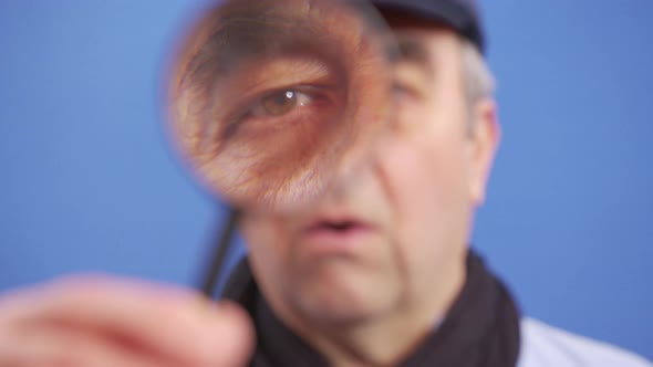 A Funny Mature Man Looks at the Camera with a Magnifying Glass Looking for Valuable Information