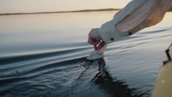 Person Hand Tries to Launch Paper Ship on Lake Water Closeup