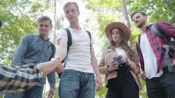 Bottom Angle View of Confident Young Man Giving Hand To Fallen Friend in Sunny Forest. Group of