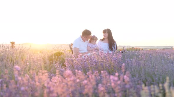 Beautiful Young Family Dad and Mom with Little Girl Sitting on Picnic at Sunset in Lavender Field