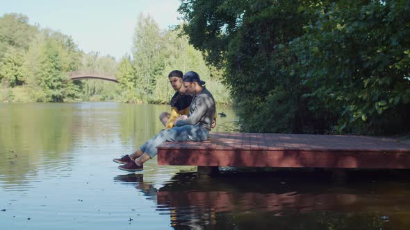 Positive Same-sex Couple Relaxing on Pier By Lake