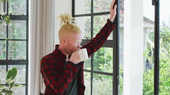 Thoughtful albino african american man with dreadlocks drinking coffee and looking at the window