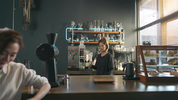 4K Asian woman barista making iced matcha green tea latte serving to customer at cafe