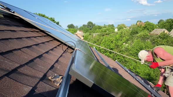 Worker Installs Solar Panel on Roof of Small Home Secured with Rope