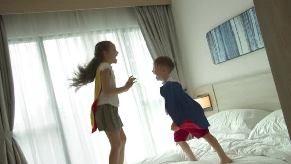 Children Playing Superheroes are Jumping in Room on Bedin Children's Room Two Children in Red and
