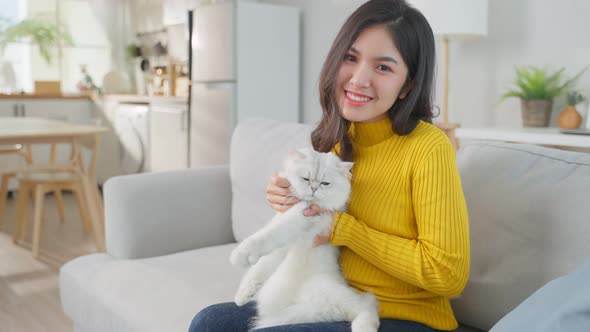 Portrait of beautiful woman sitting on sofa holding little cat with happiness in living room.