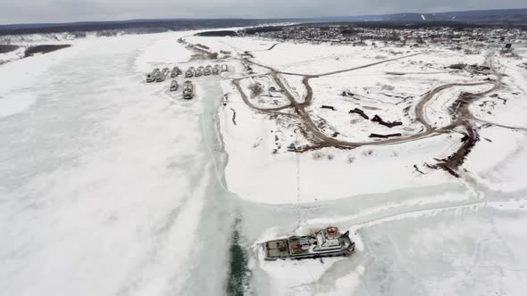 A flight over a frozen river and a view of ships and ports covered in ice and snow.