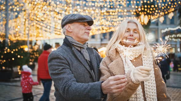 Outdoor Portrait of Happy Senior Couple in Love Holding Bengal Lights and Singing Xmas Songs in City