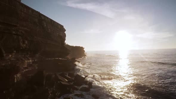 Epic aerial drone view of a cliff at sunset over a  village near Lisbon while the waves splash again