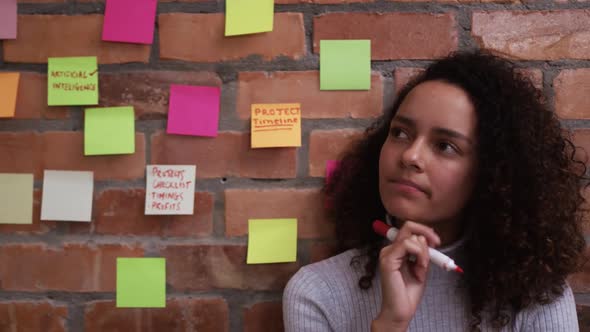 Thoughtful creative businesswoman writing on sticky notes in modern office