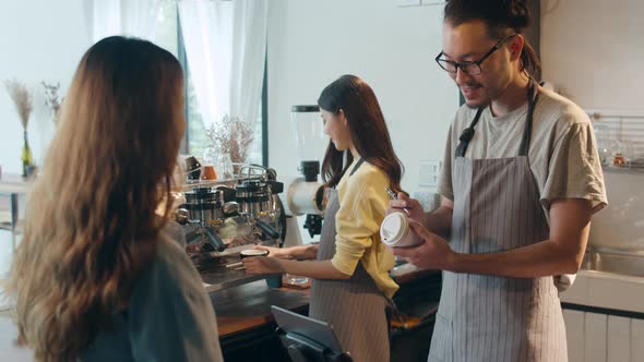 Young Asia female barista waiter taking order from customer standing behind bar.