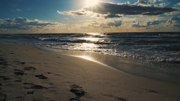 Sunset Behind Clouds Over Sea Waves and Sandy Beach