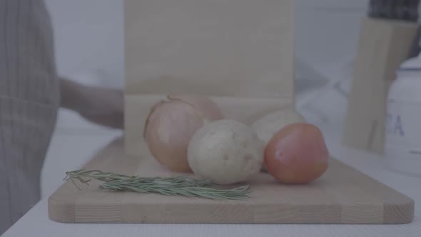 a woman puts tomatoes on a cutting board with potatoes and onions