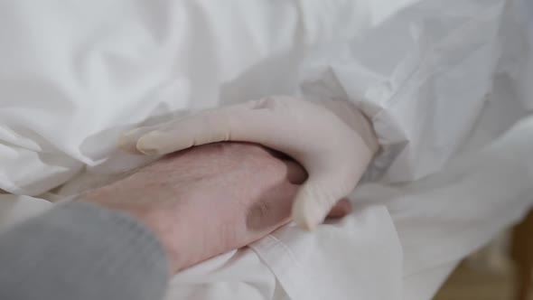 Closeup of Female Hand on Protective Gloves Taking Hand of Ill Male Patient Lying on Medical Couch