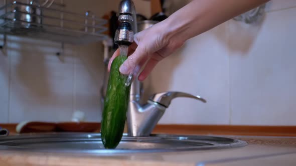 Female Washing Green Cucumber with Running Water From a Tap in a Modern Kitchen