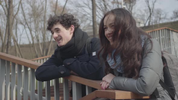 Portrait of Young Caucasian Students Chatting and Laughing in City Park. Beautiful Girl and Handsome