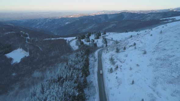 Drone Follows Big Rig Semi Truck Driving on Winding Winter Snow Road with Snowy Forest.