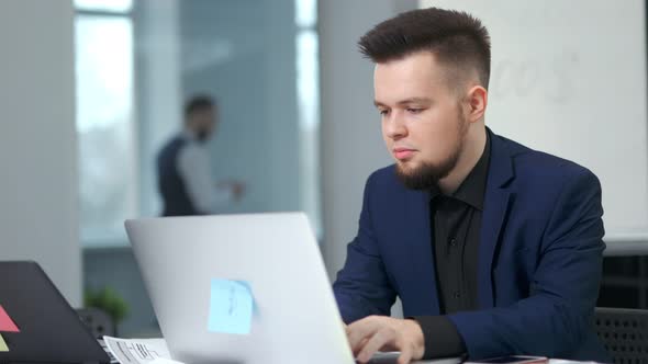 Portrait Confident Stylish Young Businessman Wearing Suit Using PC Sitting at Table in Modern Office