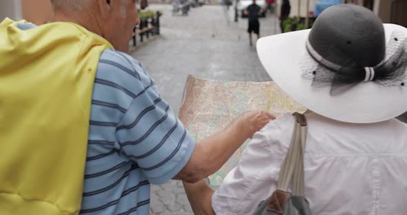 Back View of Senior Tourists Walking with a Map in Hands Looking for Route