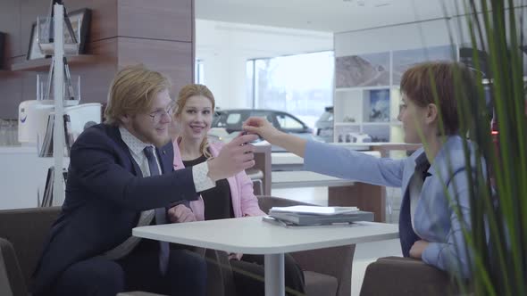 Saleswoman in a Stylish Suit Transmitting the Keys To the New Car Happy Successful Business Couple