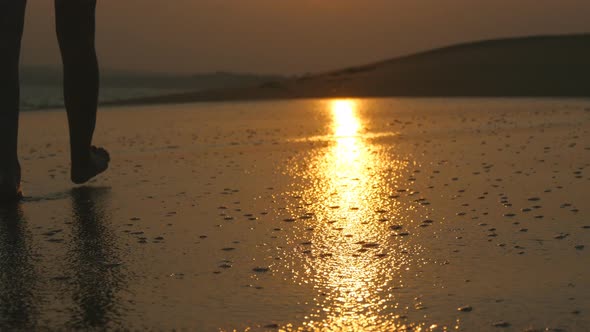 Legs of Young Woman Going Along Ocean Beach During Sunrise. Female Feet Walking Barefoot on Sea