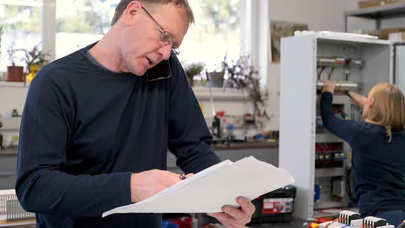 Electrician having phone call while checking circuit plan