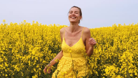 Woman Running and Swaying Her Hands Across the Field of Canola Flowers