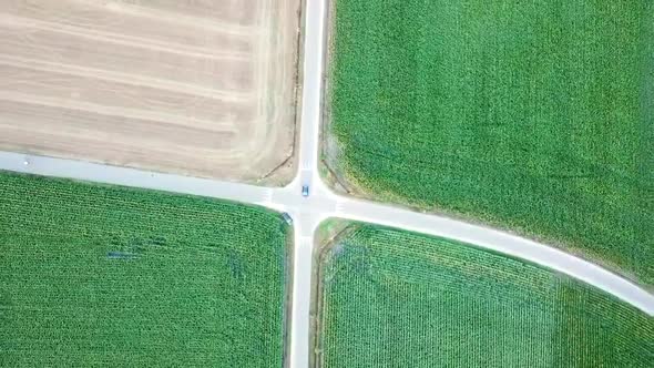 A single car driving on a crossroad with green fields, drone helicopter view perfect square plus sha