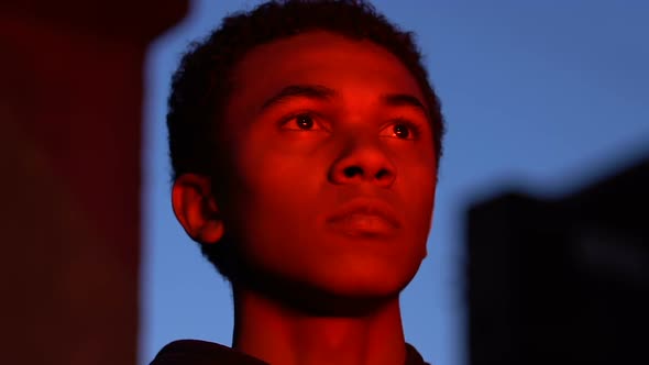 Male teenager in red lights looking at burning fire at night