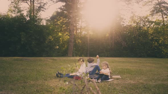 Pupils and Cute Girl with Books Rest on Lawn at Sunlight