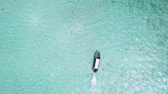 Motor boat sailing in turquoise ocean waters, overhead drone shot.