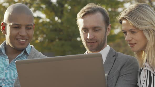 Sliding Shot of Three Business Colleagues Using Laptop at the Park