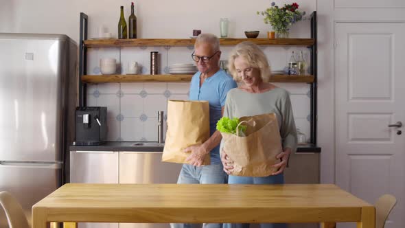 Smiling Mature Couple Unpack Bags with Groceries in Kitchen After Shopping