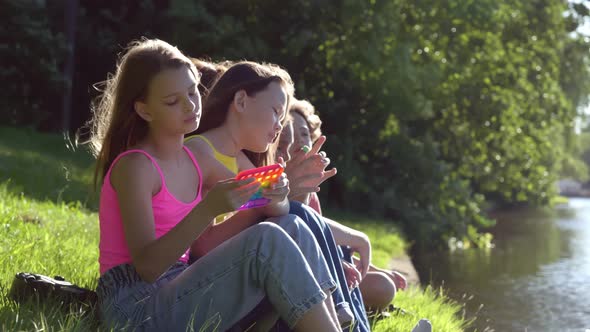 Side View of Teenage Kids Play with Trendy Sensory Toy Pop It Outdoors on Grass Near River